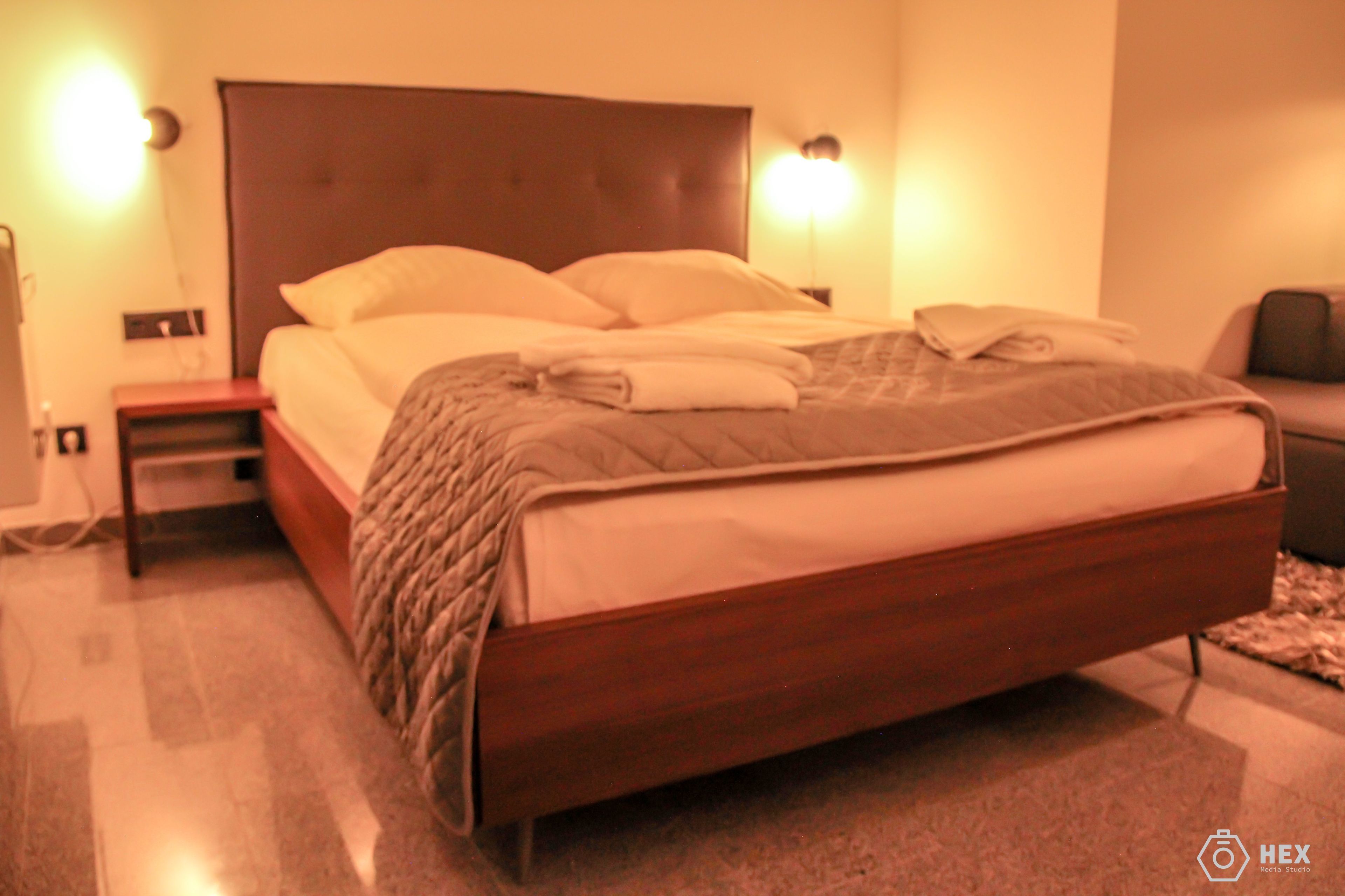 Un letto ben rifatto con struttura in legno e testiera, affiancato da due lampade da comodino e un piccolo tavolino.