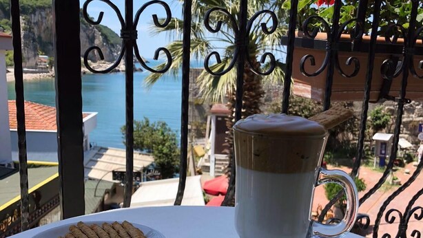 Una mesa con una taza de café y un plato de galletas, con vista a un paisaje costero.