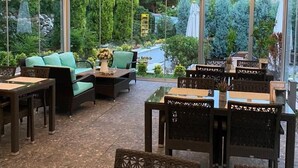 Un área de estar interior con mesas y sillas, ventanas amplias y vista a zonas verdes exteriores.