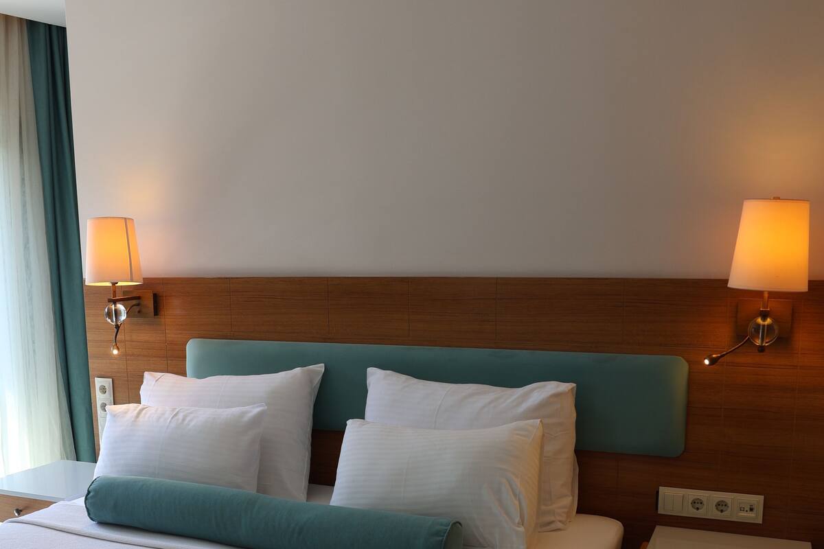 A hotel room with a large bed, two bedside lamps, a wooden headboard, and a nightstand.