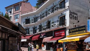 Un edificio de varios pisos con balcones, una señalización visible que dice 'Sardinia Otel', y escaparates con letreros que indican 'Amasra Tadinda' y 'Lokum - Helva'.