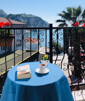A table with a book and a cup on a balcony overlooking a coastal area with a mountain in the background. - Sardinia Hotel (Amasra)