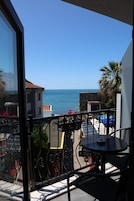A balcony with a view of the sea, a table, and chairs.