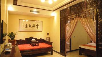 Une chambre traditionnelle avec un grand lit, un plus petit lit, un bureau agrémenté d’une plante et une œuvre calligraphique encadrée accrochée au mur.