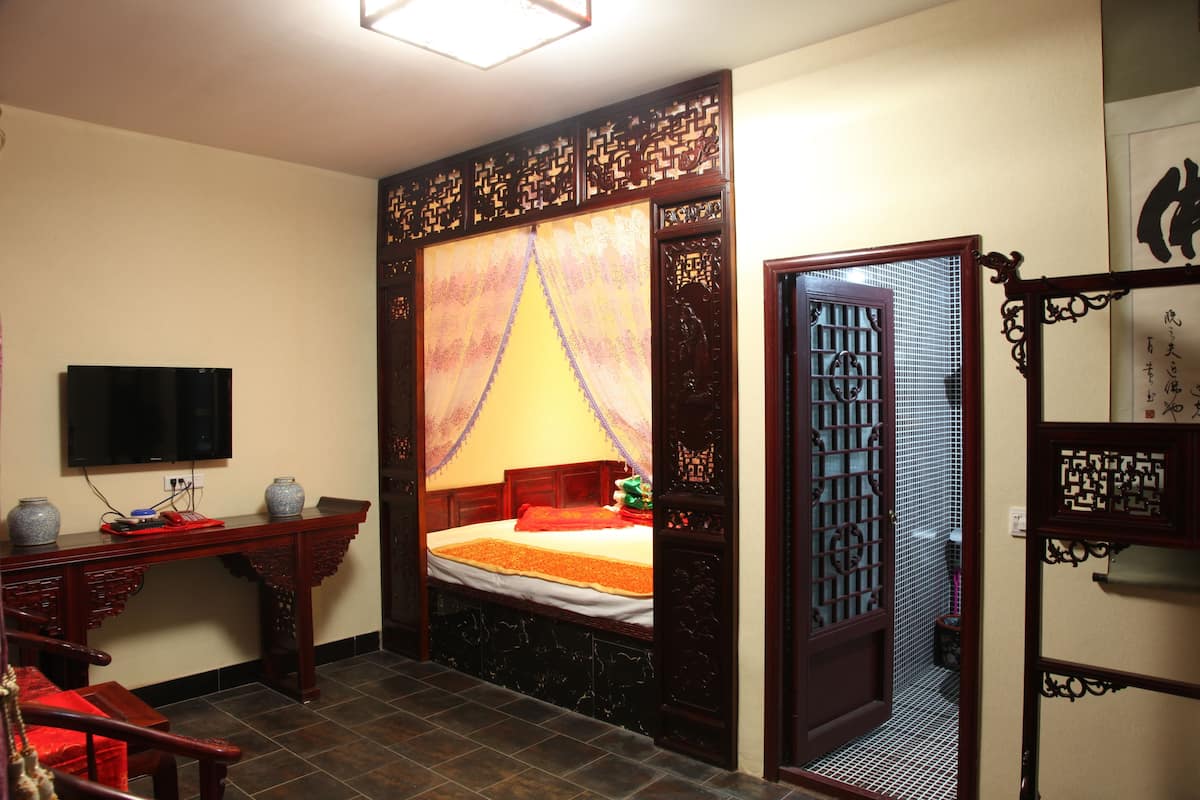 A traditional room with a bed, a desk, a television, and a decorative screen.