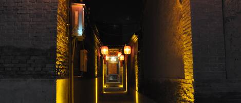 A narrow alleyway with traditional lanterns hanging from the ceiling, flanked by brick walls.