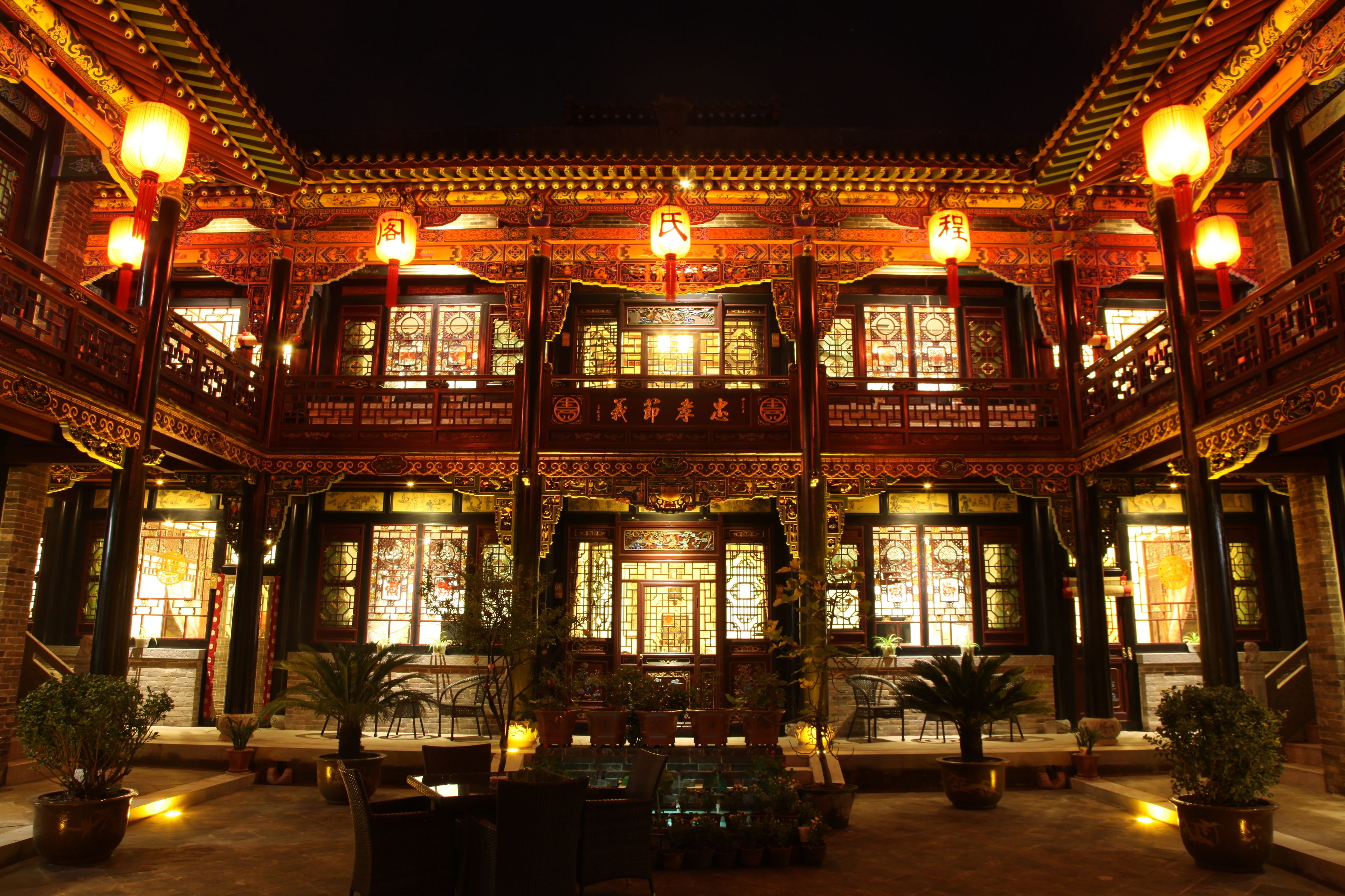 Un bâtiment traditionnel chinois, doté d’une architecture richement décorée, de grandes fenêtres et de plantes en pot.