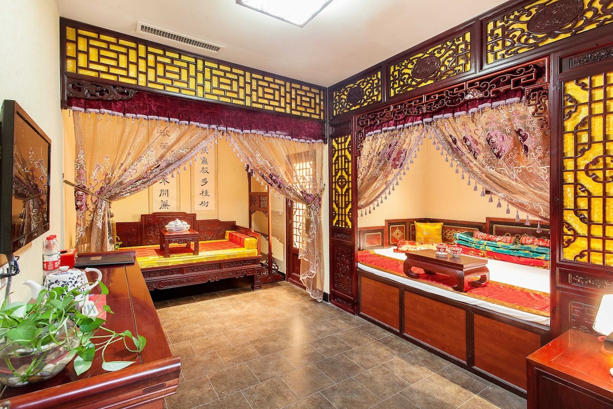 A traditional room with a bed, a sofa, and a desk. There are decorative screens and curtains.