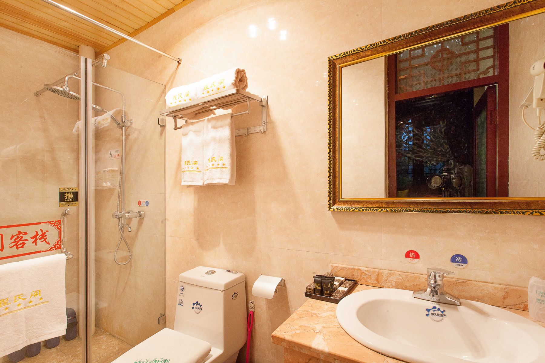 A bathroom with a glass shower, a toilet, a sink, and a mirror with a decorative frame.