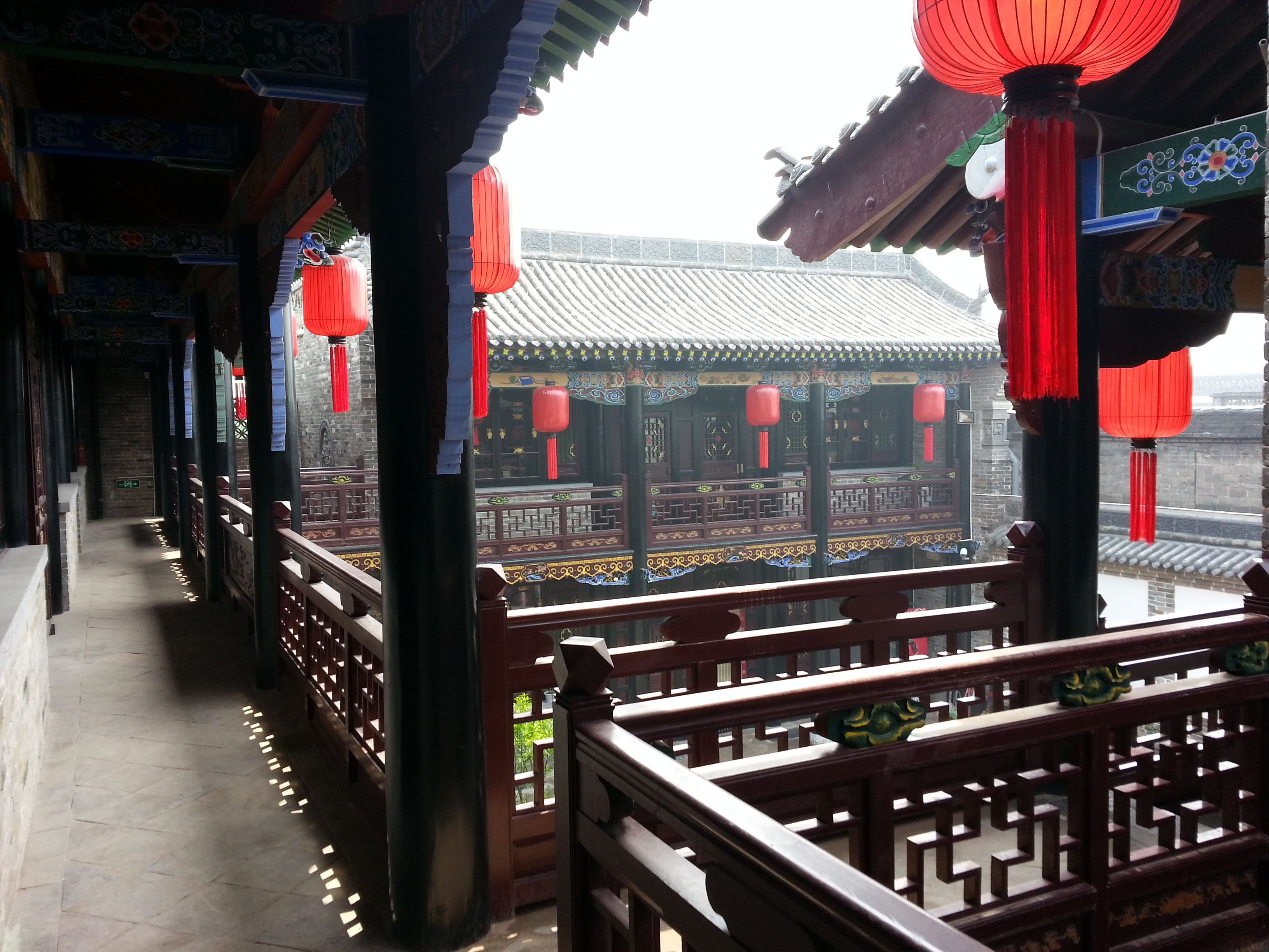 A traditional architectural corridor with wooden railings and red lanterns.