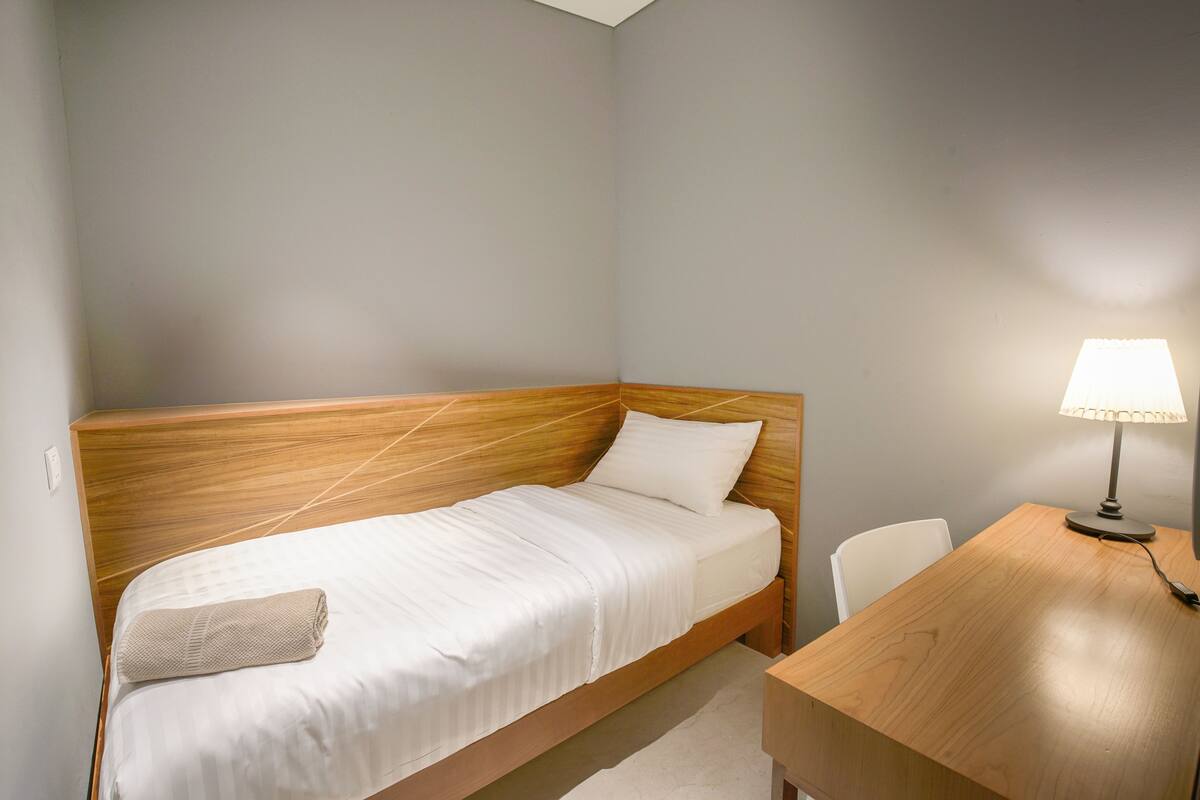 Una cama individual con cabecera de madera, una mesita de noche y una lámpara.