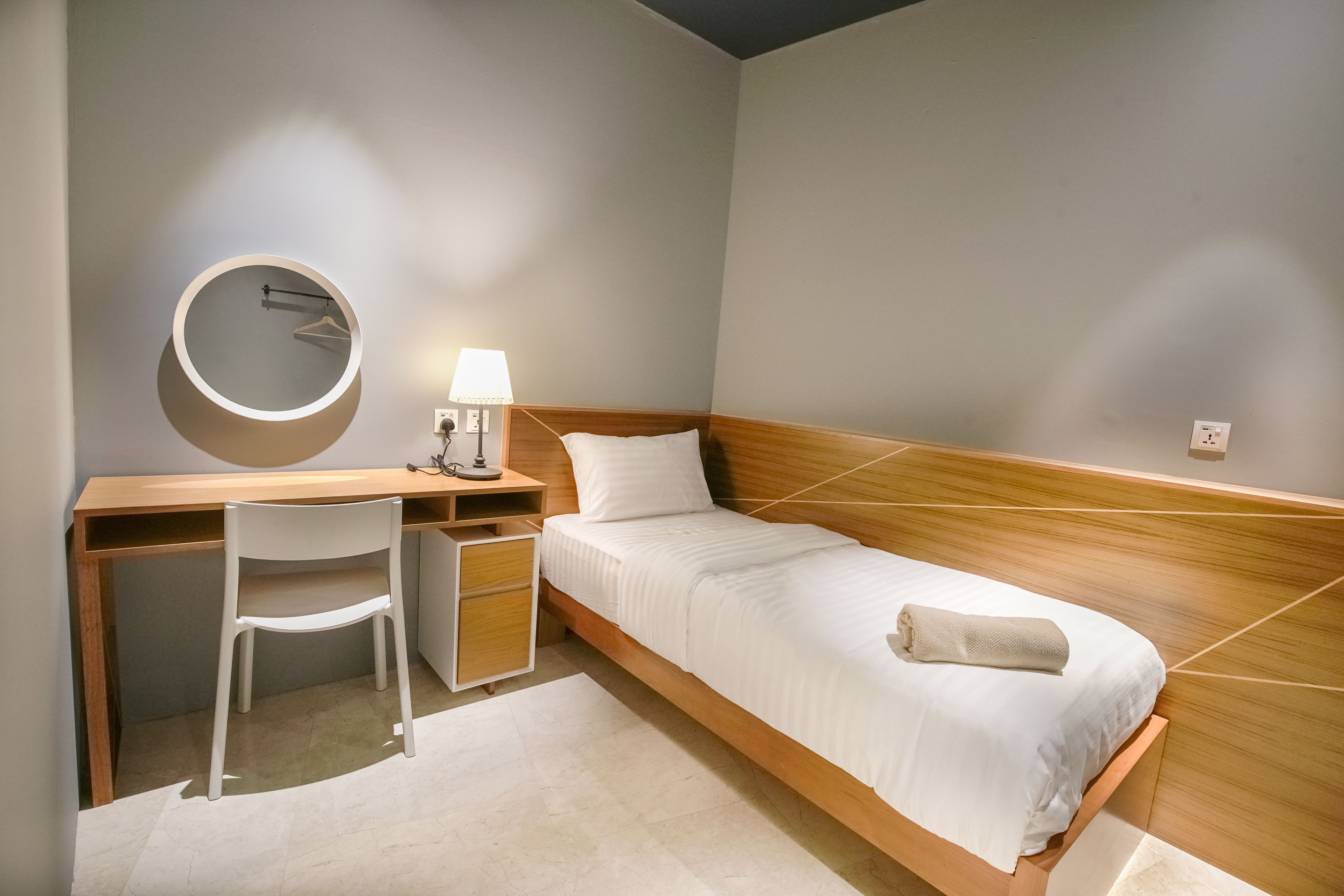 A compact bedroom with a wooden bed, a desk with a chair, and a bedside lamp.
