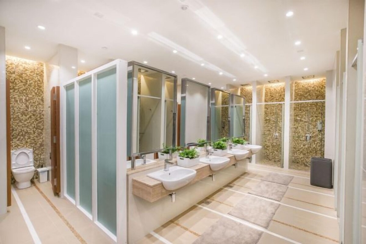 A modern bathroom with a row of sinks, a toilet, and a shower area.