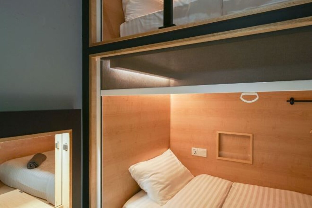 A compact room with a bunk bed and a single bed, wooden headboard, and a small bedside table.