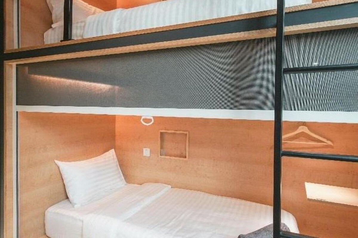 A bunk bed room with a mattress and pillows on the lower bunk, a small shelf, and a wall-mounted hanger.