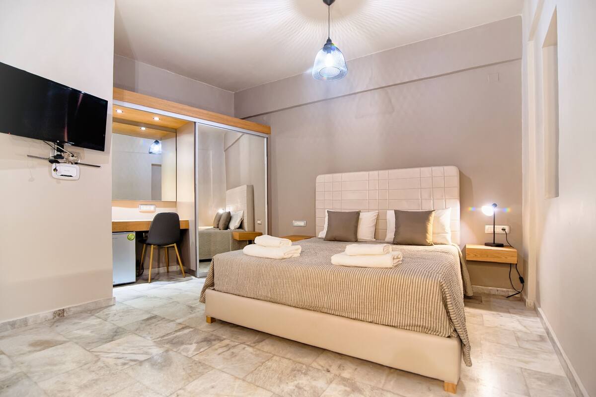 Un dormitorio moderno con una cama grande, mesitas de noche, un escritorio y un televisor montado en la pared.