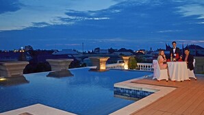 A poolside dining area with a view of the city skyline at dusk. - The Axana Hotel (Padang)