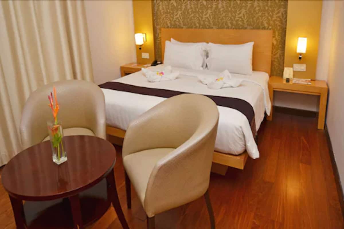 A hotel room with a bed, two chairs, a small table, and two bedside lamps.