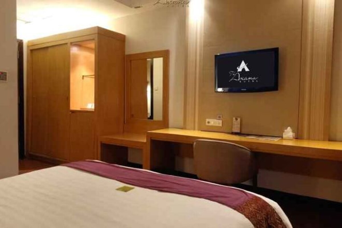 A hotel room with a bed, a desk, a chair, a wardrobe, and a television on the wall.