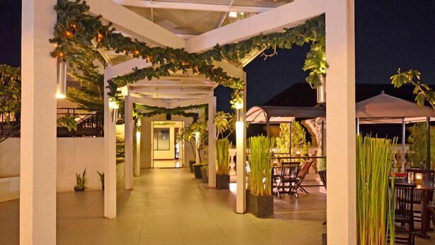 An outdoor covered patio area with columns, potted plants, and tables. - The Axana Hotel (Padang)