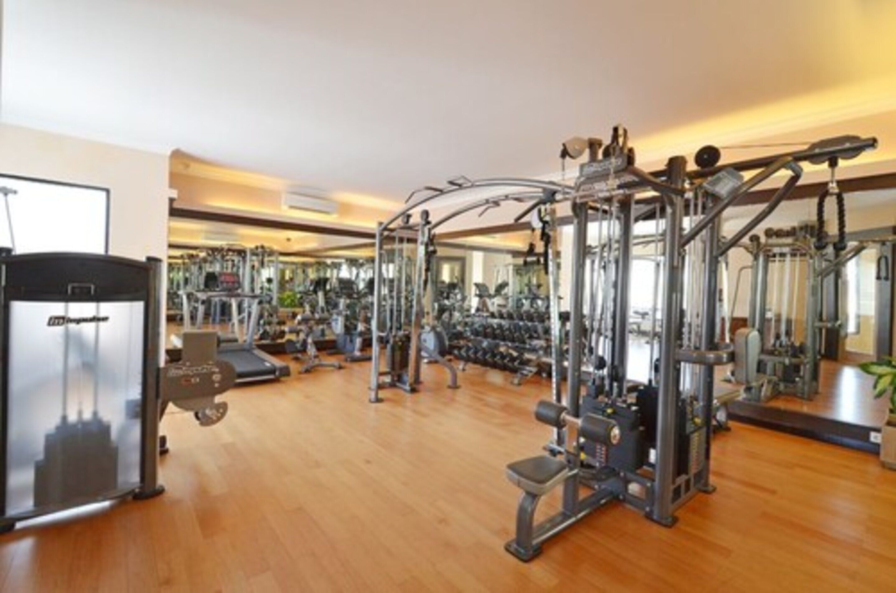Une salle de sport équipée de divers appareils d’exercice, d’un tapis de course et d’un mur recouvert de miroirs.