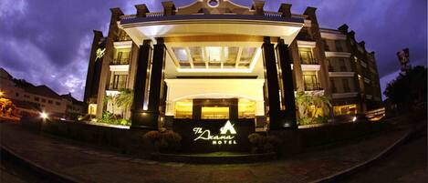 Un hotel con una entrada destacada, un cartel grande con el nombre del hotel y una fachada bien iluminada.