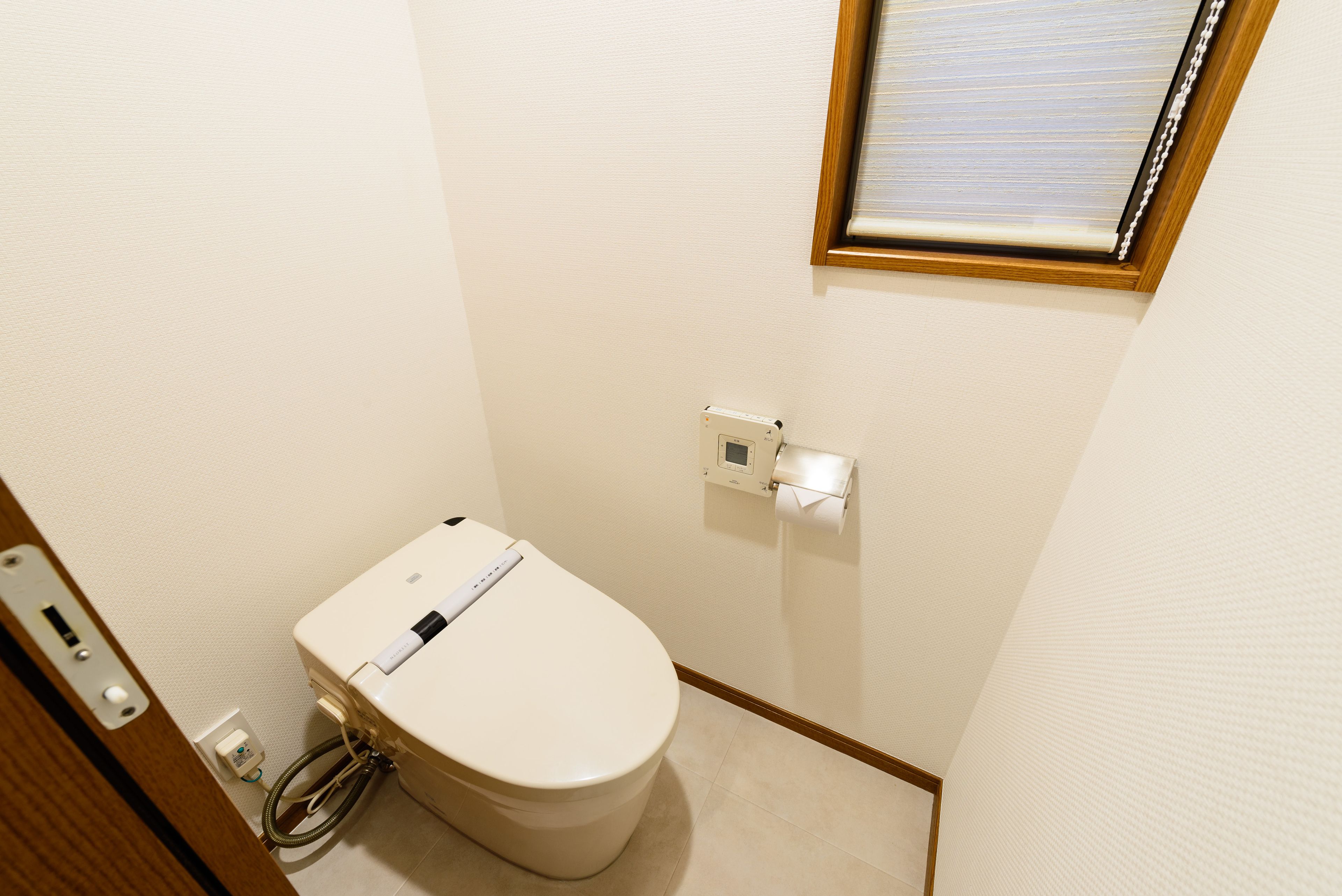 A small, clean bathroom with a toilet, a toilet paper holder, and a power outlet.