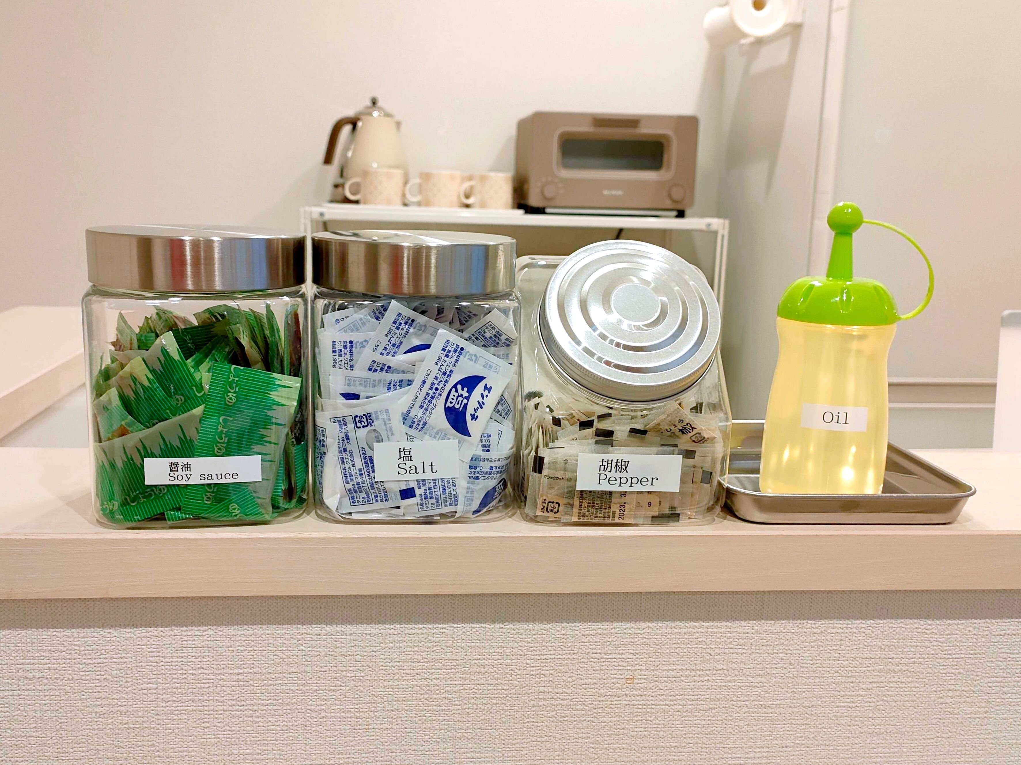Four labeled containers on a shelf: soy sauce, salt, pepper, and oil.