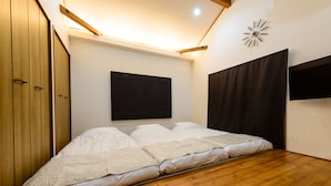 Un dormitorio con piso de madera, una cama con ropa blanca, un cabecero oscuro, un reloj de pared y un armario de madera.
