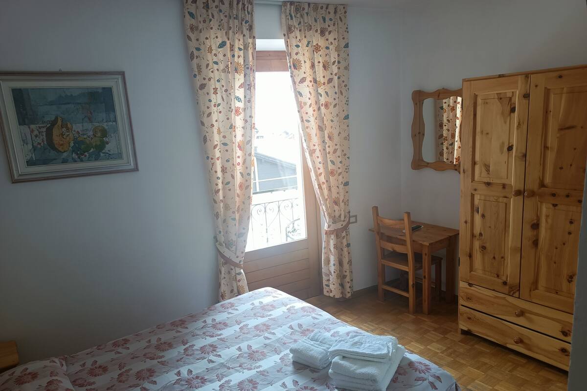 Ein Schlafzimmer mit einem Bett, einem Holzschrank, einem Sessel, einem Schreibtisch und einem Fenster mit Vorhängen.