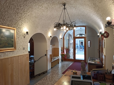 A hallway with a rustic stone ceiling, wooden paneling, and a chandelier. There are arched doorways leading to other rooms.