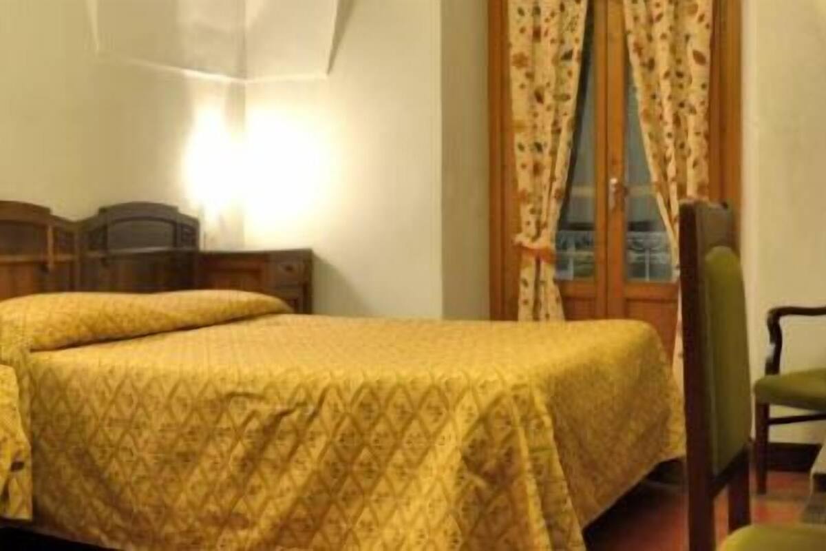 Ein Zimmer mit zwei Einzelbetten, einem Schreibtisch mit Stuhl, einem Spiegel und einem Fenster mit Vorhängen.