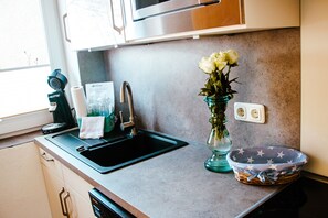 A kitchen with a stainless steel sink, a vase with flowers, and a basket with a star pattern. - Meislahnhof Fehmarn (Fehmarn)