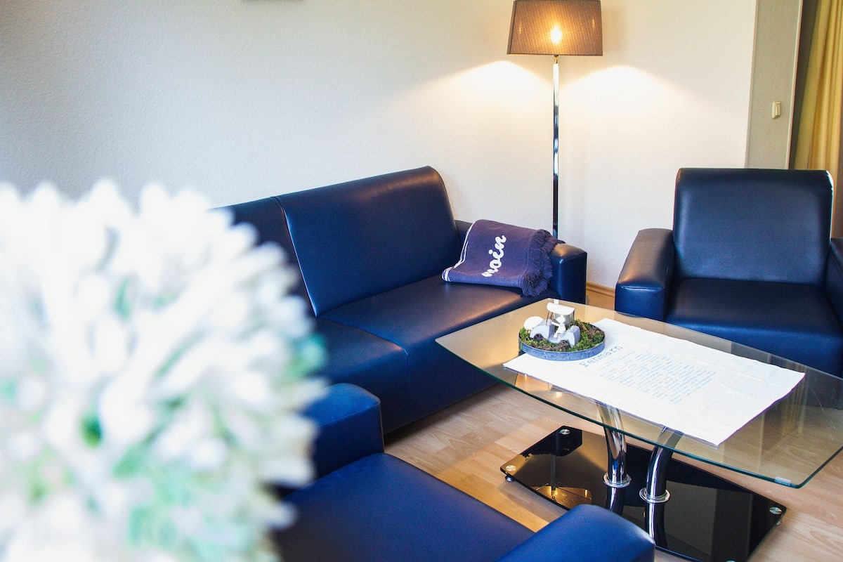 Une chambre d’hôtel moderne avec un canapé bleu, une table basse en verre et un lampadaire.