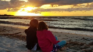 Zwei Personen sitzen am sandigen Strand und blicken während des Sonnenuntergangs auf den Ozean.