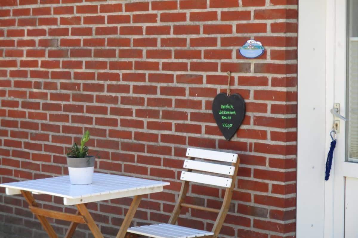 Un mur de briques avec une porte blanche, une petite table sur laquelle est posée une plante en pot et une chaise en bois.