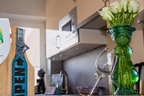 A kitchen counter with a green vase containing white flowers, a wine glass, and a blue and black tool. - Meislahnhof Fehmarn (Fehmarn)