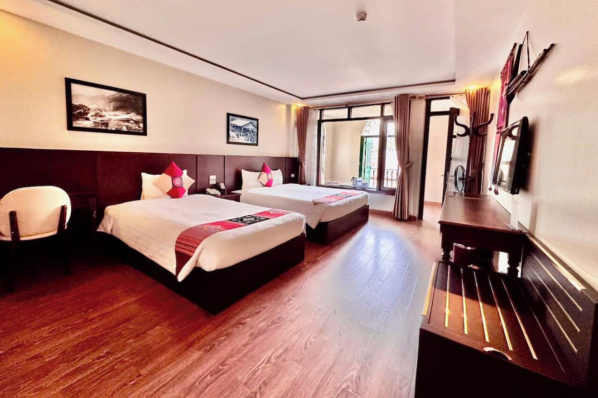 Habitación de hotel con dos camas, un escritorio, una silla y un ventanal con cortinas.