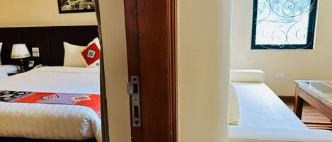 Una habitación de hotel con cama, mesita de noche, ventana con herrajes decorativos y un cuadro colgado en la pared.