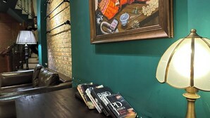 A cozy lounge area with a leather couch, a table with books, a lamp, and a framed painting on the wall. - Sapa Centre Hotel (Sa Pa)