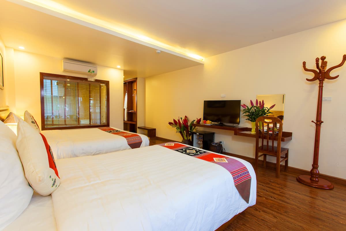 Una habitación de hotel con dos camas, un escritorio con computadora, un televisor y un perchero.
