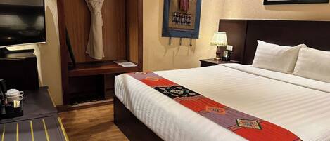 A hotel room with a large bed, a television on a desk, a coat rack, and a framed picture on the wall.