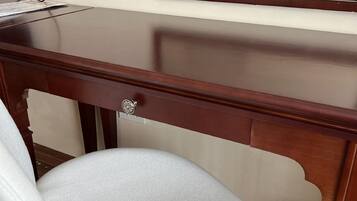 Un escritorio de madera con una silla blanca, un cajón y un espejo encima.