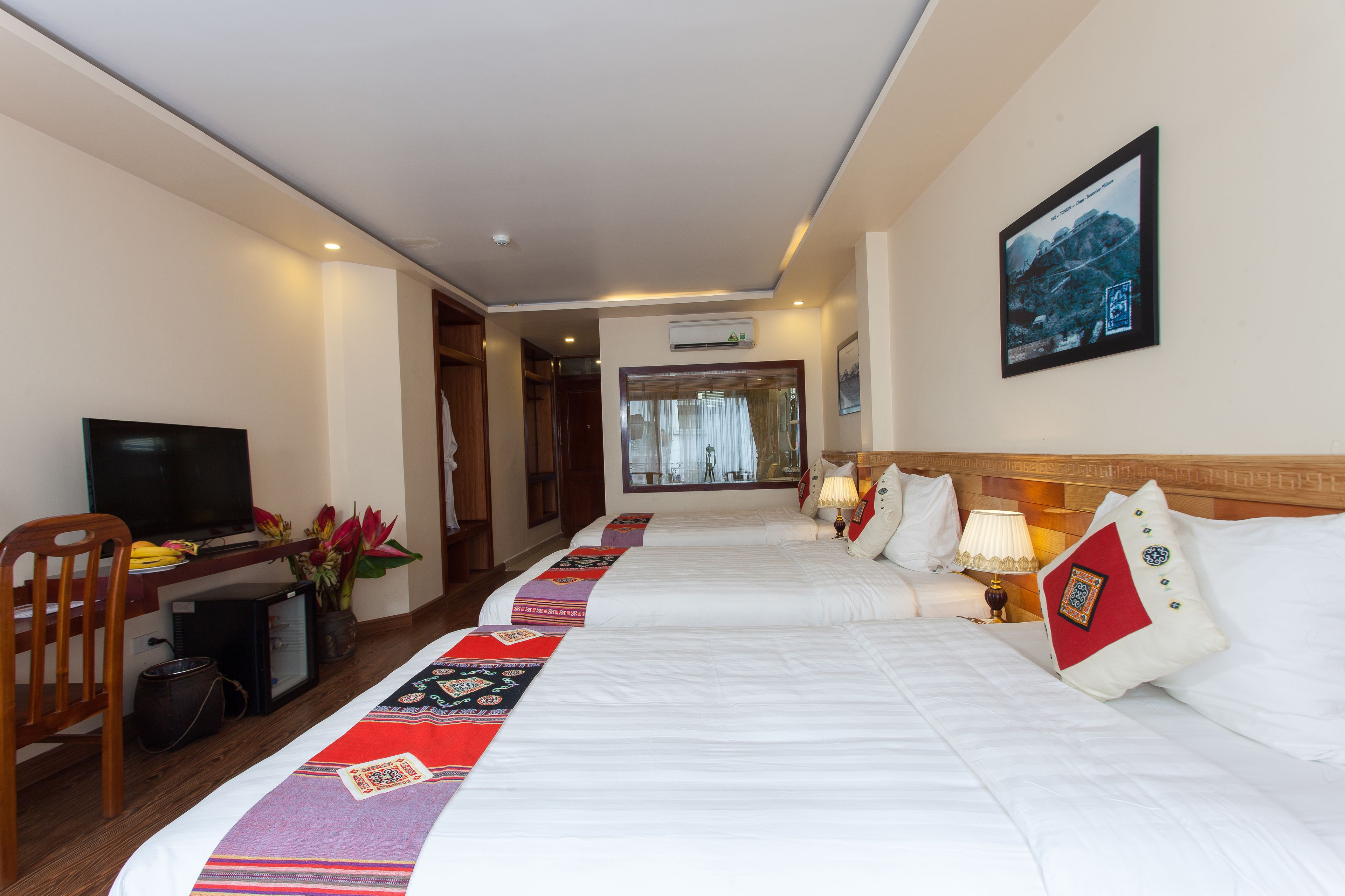 A hotel room with two beds, a desk with a television, a chair, and a window with curtains.
