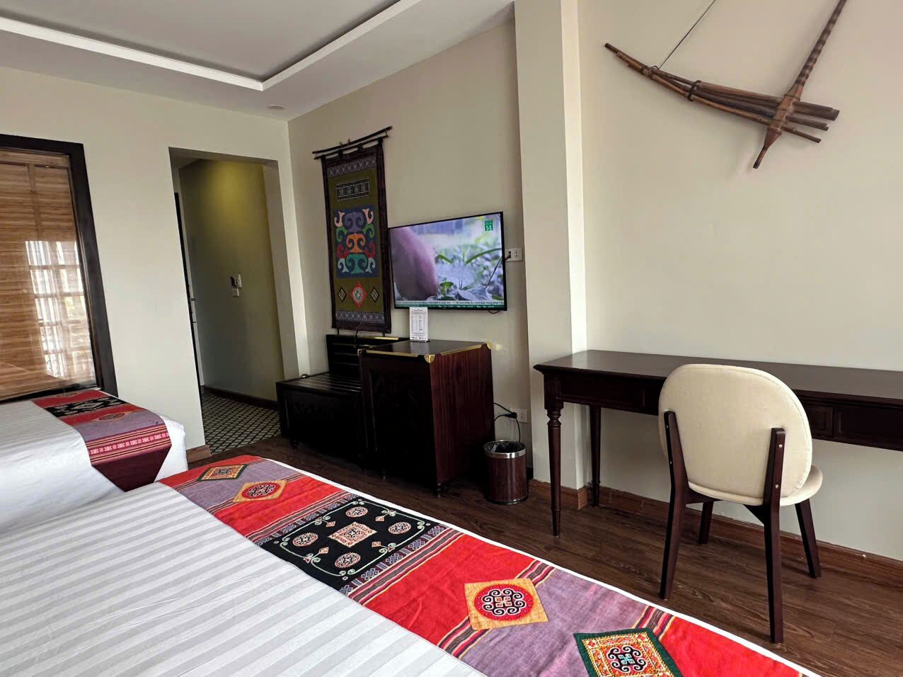 A hotel room with a bed, a desk, a chair, a television, and a decorative wall hanging.