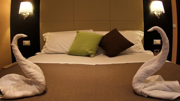 Habitación de hotel con una cama, dos lámparas de pared y dos toallas con forma de cisne sobre la cama.