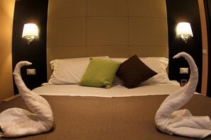 Una camera d'albergo con un letto, due lampade fissate al muro e due asciugamani a forma di cigno sul letto.