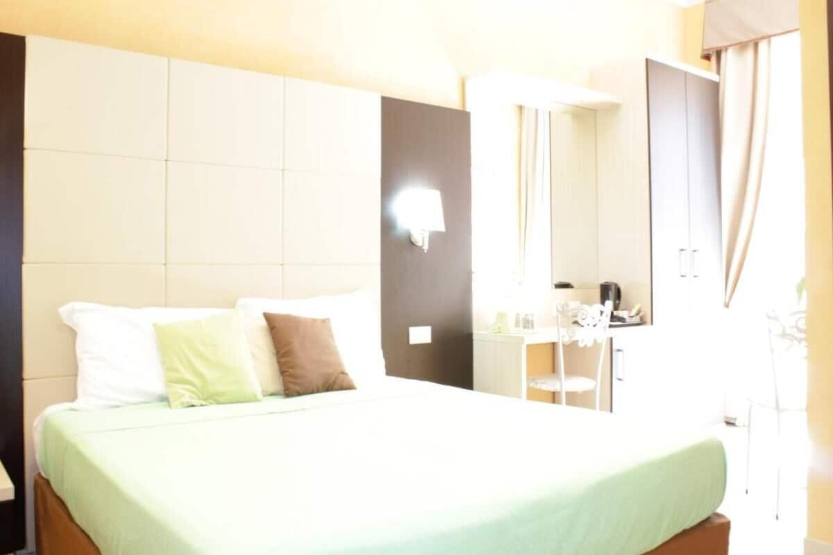 A hotel room with a bed, a desk, and a mirror.