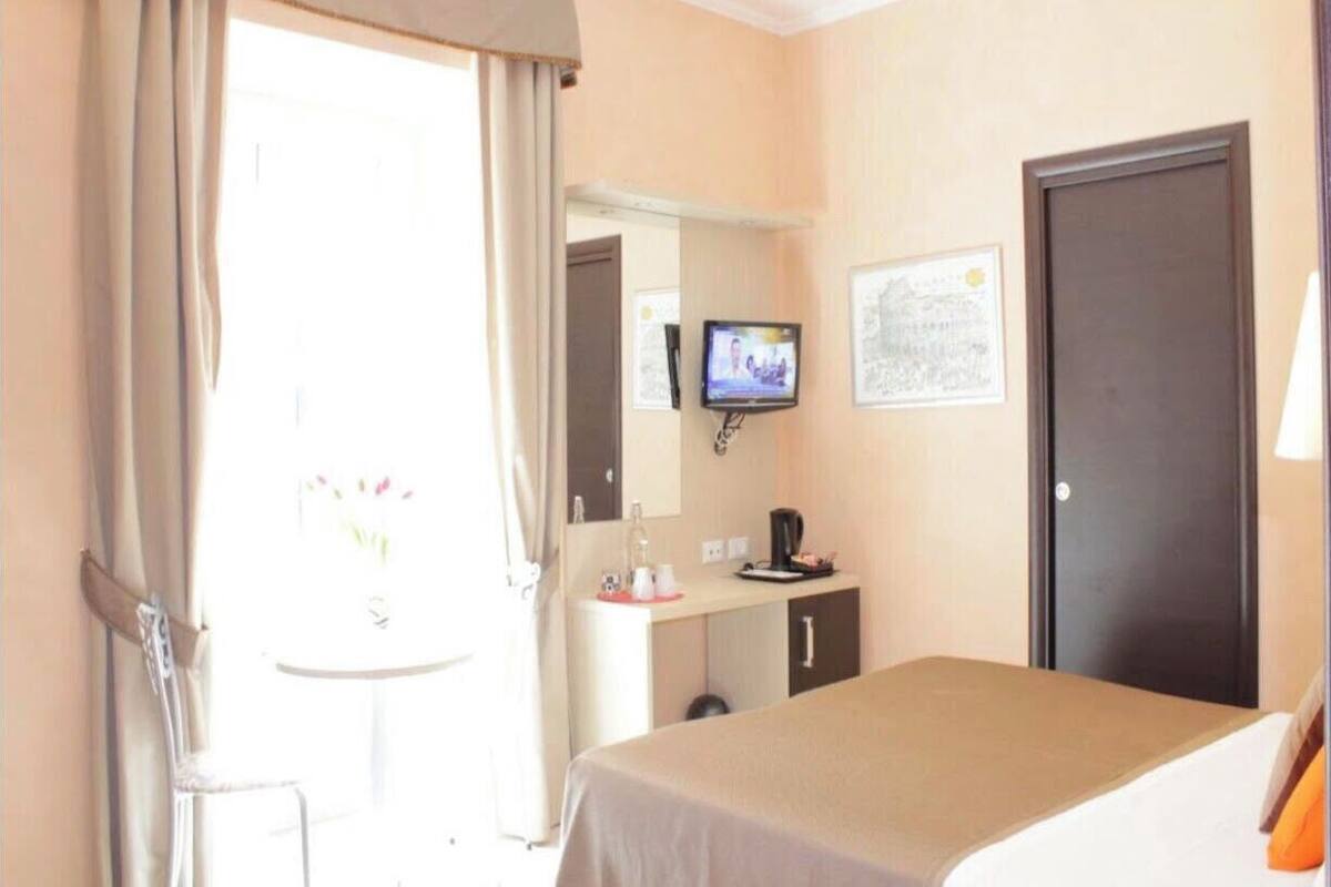 A hotel room with a bed, a desk with a chair, a television, and a door.