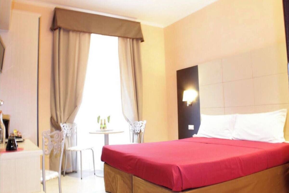 A hotel room with a bed, a desk, a chair, and a small table with a lamp.